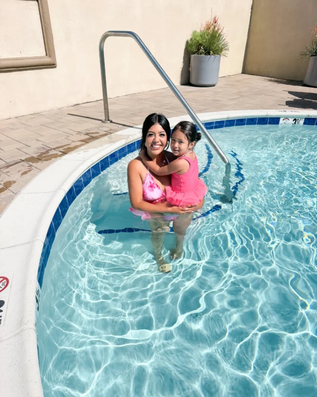 A woman and a child in a small, curved swimming pool with blue tiles.